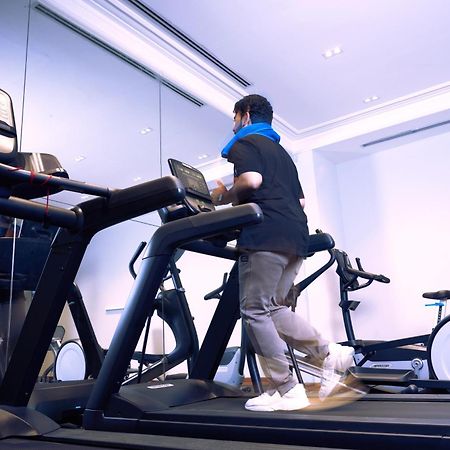 Makarem Ajyad Makkah Hotel Мека Екстериор снимка The photo shows a person exercising on a treadmill in a modern gym or fitness room. The individual is wearing a blue neck support while jogging on the treadmill, which is set against a backdrop of large mirrors. There are also additional exercise equ