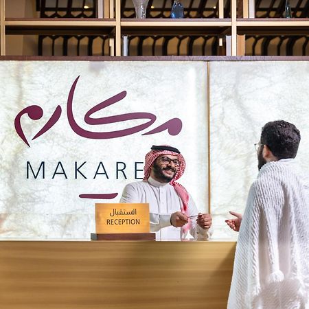 Makarem Ajyad Makkah Hotel Мека Екстериор снимка The photo depicts a reception area in a hotel or establishment named "Makarem." In the image, a receptionist, dressed in traditional attire, is smiling and interacting with a guest who is wearing a white robe, commonly known as a thobe or ihram. The 