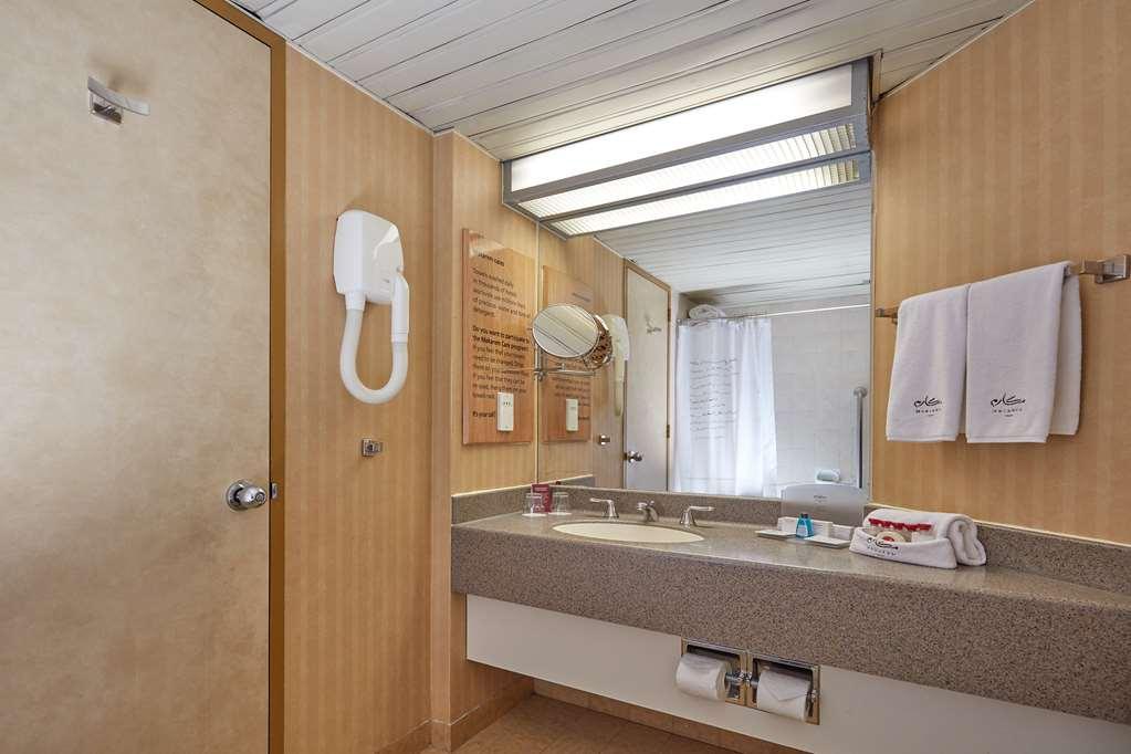 Makarem Ajyad Makkah Hotel Мека Екстериор снимка The photo shows the interior of a bathroom. It features a light-colored wall with vertical stripes and a ceiling that is white and textured. There is a gray countertop with a sink and a mirror above it. On one side, there are two white towels hanging