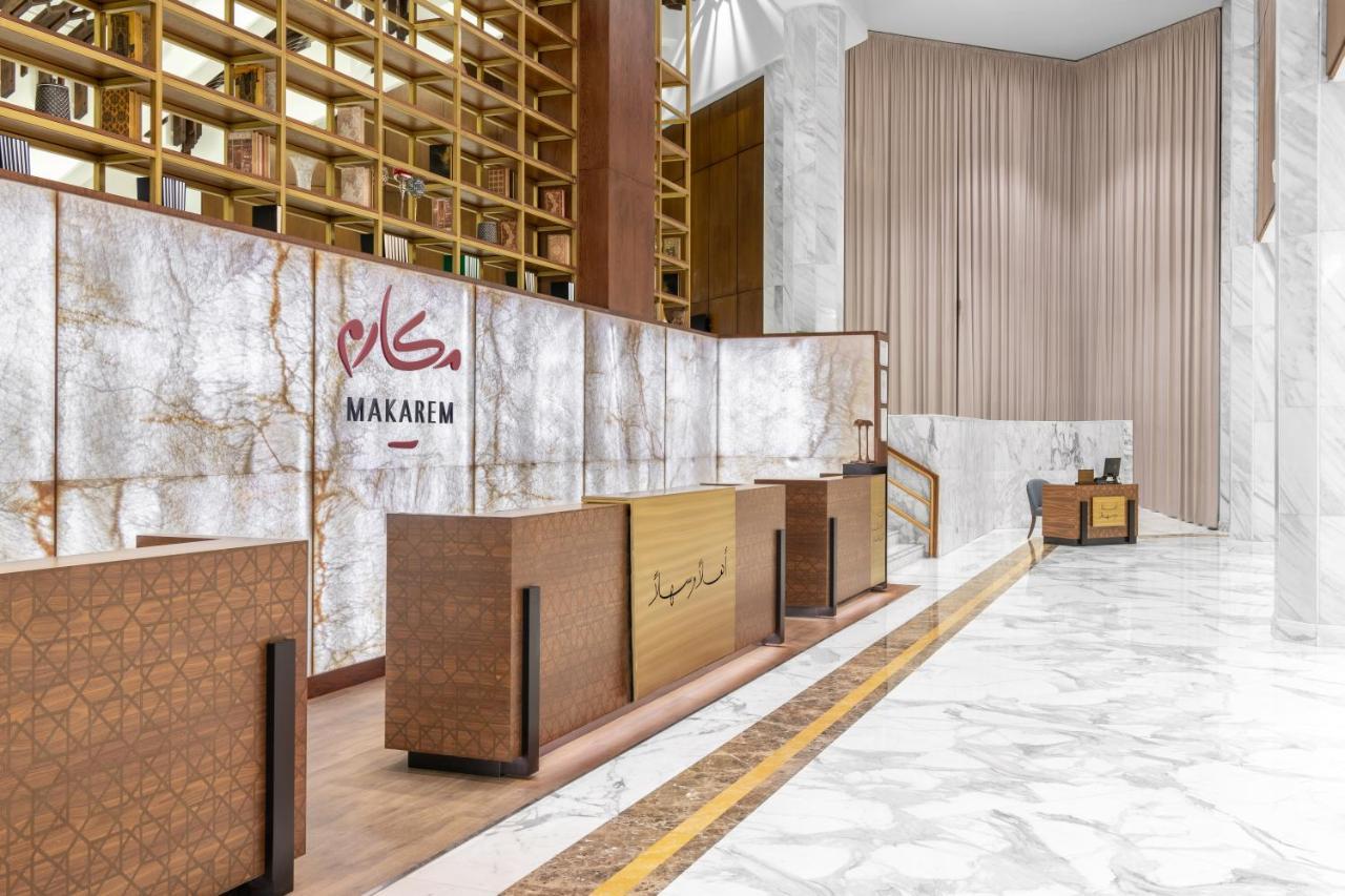 Makarem Ajyad Makkah Hotel Мека Екстериор снимка The photo shows a modern hotel reception area with a sleek design. The reception desk is made of a combination of wood and stone, featuring a warm color palette. The backdrop is adorned with a marble finish, giving a luxurious feel. Above the desk, t