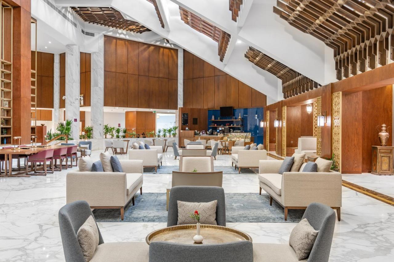 Makarem Ajyad Makkah Hotel Мека Екстериор снимка The photo depicts the interior of a modern and elegantly designed lobby or lounge area. It features a spacious layout with high ceilings, showcasing a combination of wooden elements and marble flooring. 

In the center, there are several seating arra