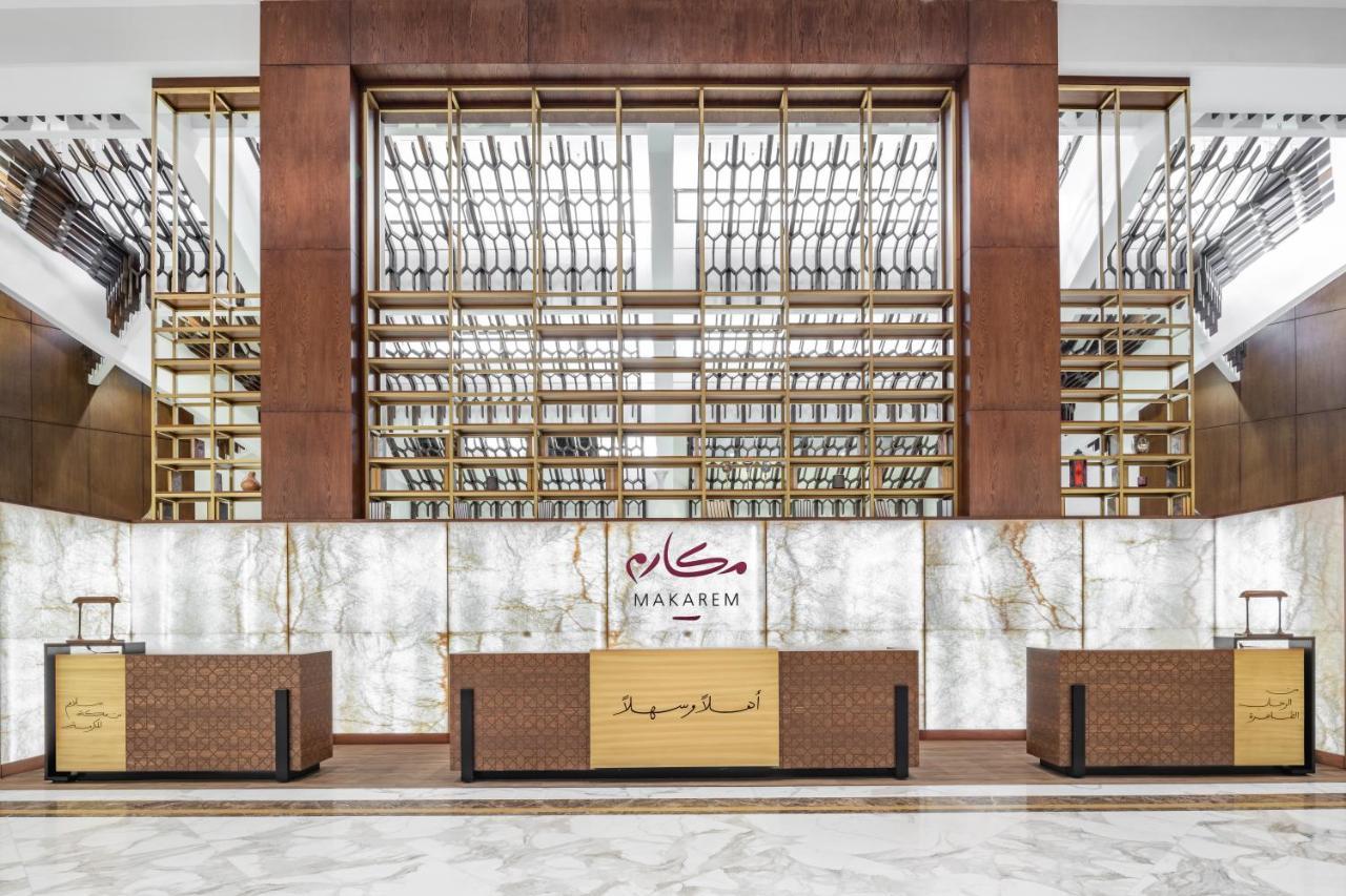 Makarem Ajyad Makkah Hotel Мека Екстериор снимка The photo shows the interior of a hotel or a reception area, characterized by a modern and elegant design. In the foreground, there are multiple reception desks with a polished finish. Behind the desks, a striking feature is a wooden wall with a geom
