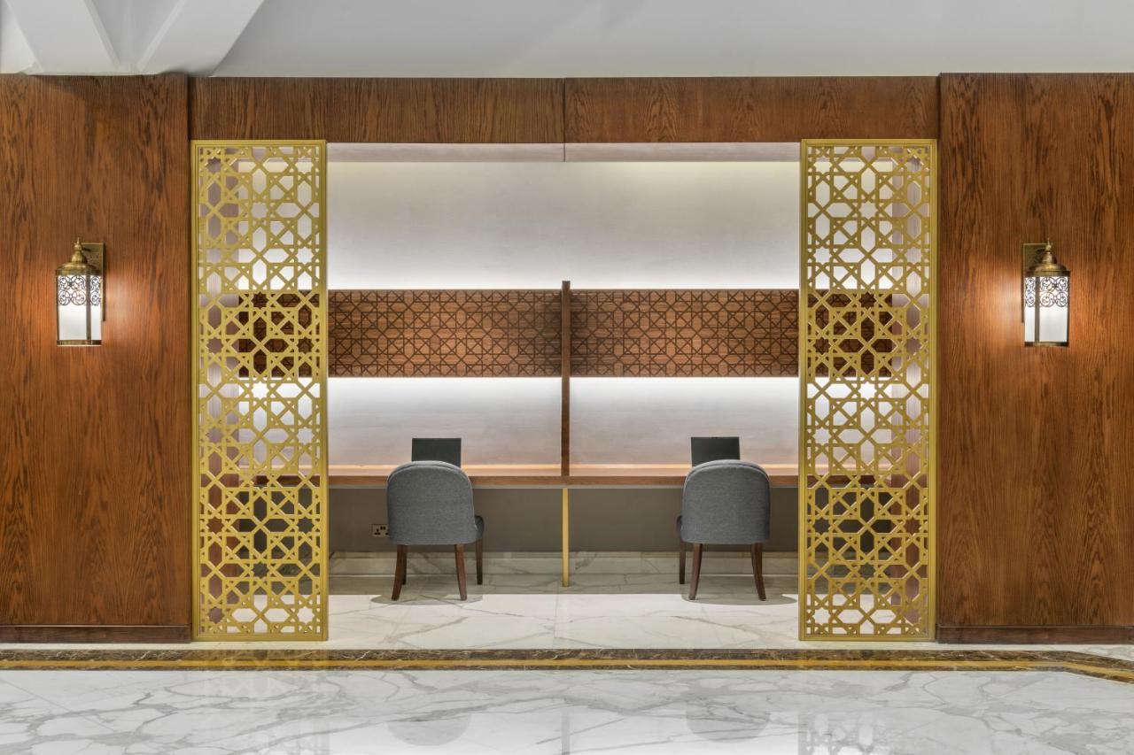 Makarem Ajyad Makkah Hotel Мека Екстериор снимка The photo shows an elegantly designed space that features a reception or working area. There are two workstations with chairs positioned in front of them. The backdrop has a decorative panel with a geometric pattern. The area is framed by ornate gold