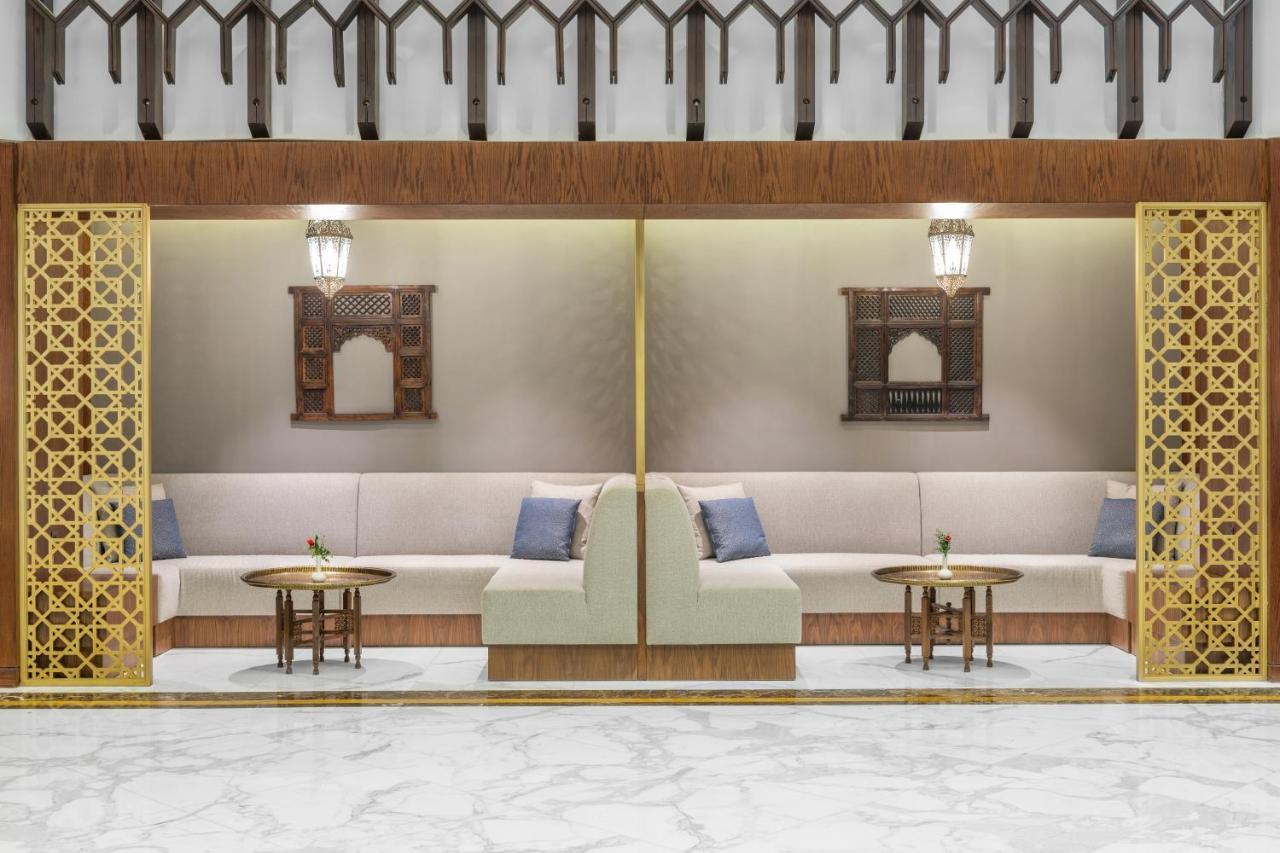 Makarem Ajyad Makkah Hotel Мека Екстериор снимка The photo depicts a modern, elegantly designed seating area. It features a pair of sofas with light-colored upholstery, accented by blue cushions. There are several small tables in front of the sofas, likely meant for drinks or decorative items. The 