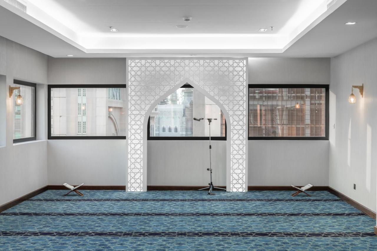 Makarem Ajyad Makkah Hotel Мека Екстериор снимка The image shows a prayer room or small mosque interior. It features a white decorative wall with an archway that is typical in Islamic architecture. The floor is covered with a blue carpet, arranged with patterned lines, likely indicating prayer spot