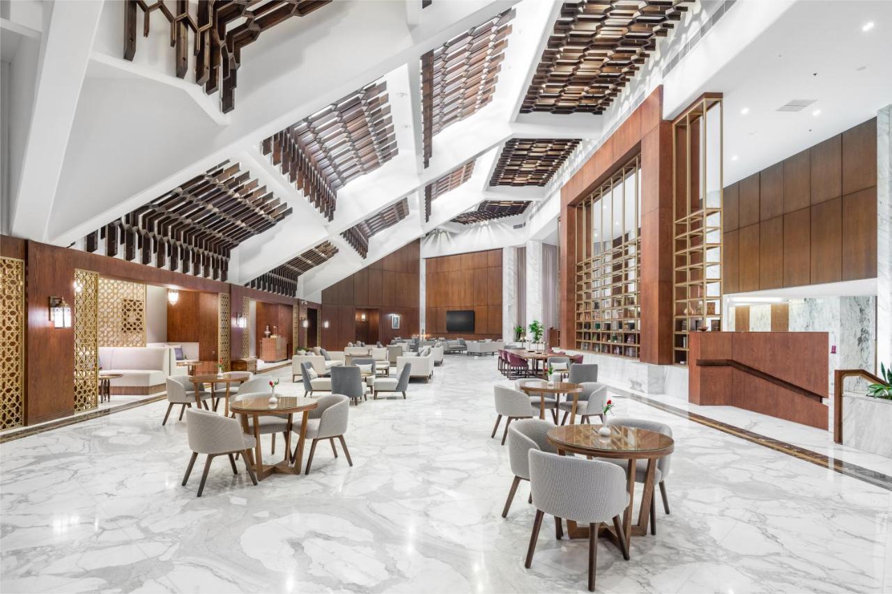 Makarem Ajyad Makkah Hotel Мека Екстериор снимка The photo shows a spacious and modern interior, likely of a hotel or a large dining area. The design features high ceilings with an interesting architectural style, including a combination of wooden elements and sleek, modern finishes. 

The floor is