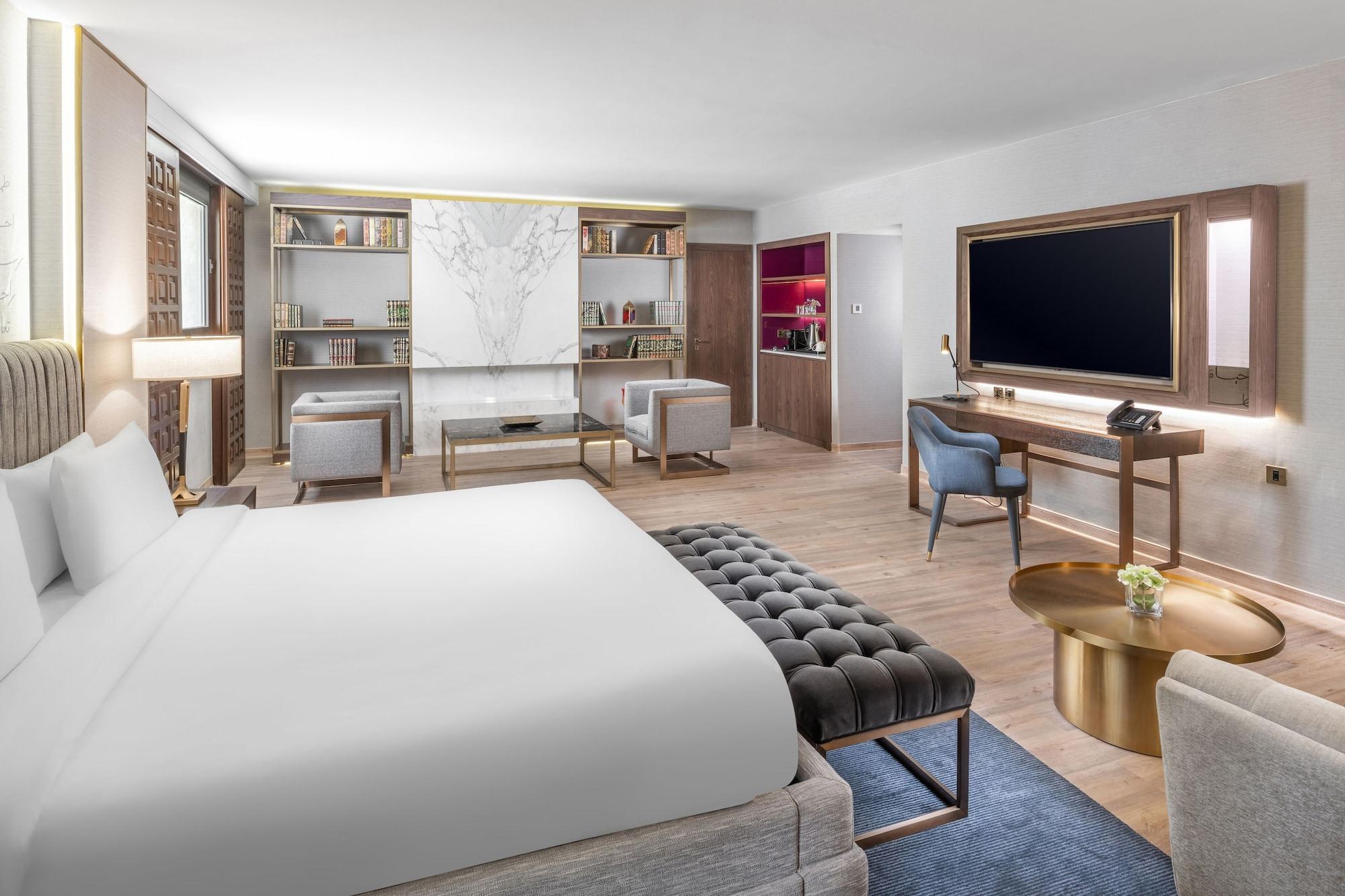 Makarem Ajyad Makkah Hotel Мека Екстериор снимка The photo shows a modern hotel room designed with a contemporary aesthetic. The room features a large bed with white bedding, complemented by a stylish tufted bench at the foot of the bed. To the side, there are two comfortable armchairs positioned a
