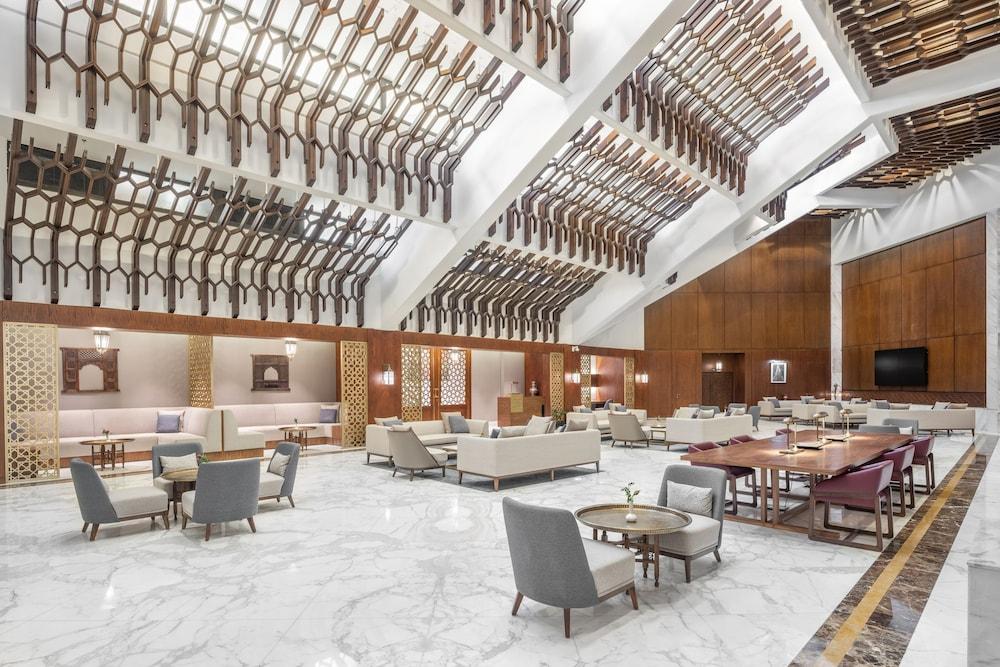 Makarem Ajyad Makkah Hotel Мека Екстериор снимка The photo shows a spacious and elegantly designed lobby area, likely within a hotel. The interior features high ceilings with a unique architectural design, showcasing wooden elements arranged in a geometric pattern. The flooring is a polished marble