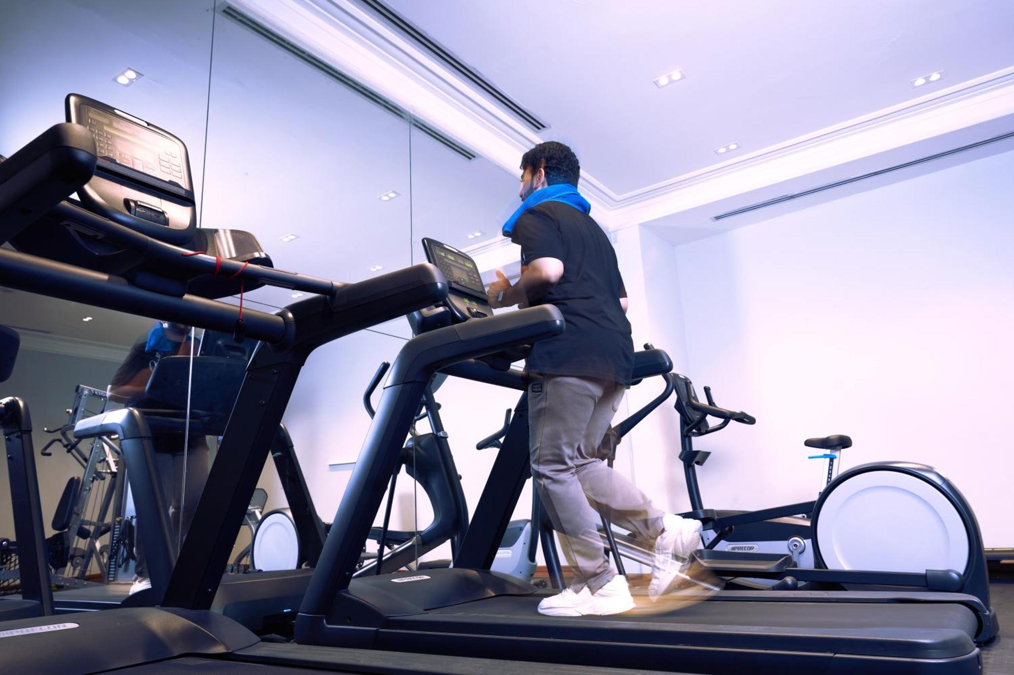 Makarem Ajyad Makkah Hotel Мека Екстериор снимка The photo shows a person exercising on a treadmill in a modern gym or fitness room. The individual is wearing a blue neck support while jogging on the treadmill, which is set against a backdrop of large mirrors. There are also additional exercise equ