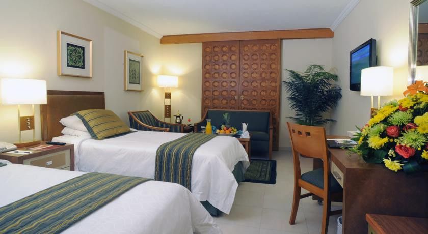 Makarem Ajyad Makkah Hotel Мека Екстериор снимка The photo shows a hotel room featuring two single beds with white linens and green and blue striped throw blankets. There is a wooden headboard behind the beds and a decorative wooden partition or wall in the background. A cozy seating area is visibl