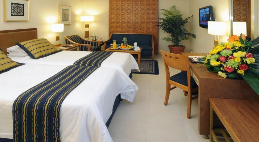 Makarem Ajyad Makkah Hotel Мека Екстериор снимка The image shows a hotel room featuring two beds with white linens and a decorative stripe along the edge. There is a seating area with two chairs and a small table, set with a breakfast spread that includes fruit and drinks. A small potted plant adds