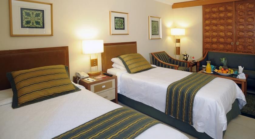Makarem Ajyad Makkah Hotel Мека Екстериор снимка The photo shows a hotel room with two twin beds, each topped with decorative green and gold striped bed runners. There is a nightstand between the beds with a lamp on it. The room features light-colored walls, framed artwork on the walls, and a small