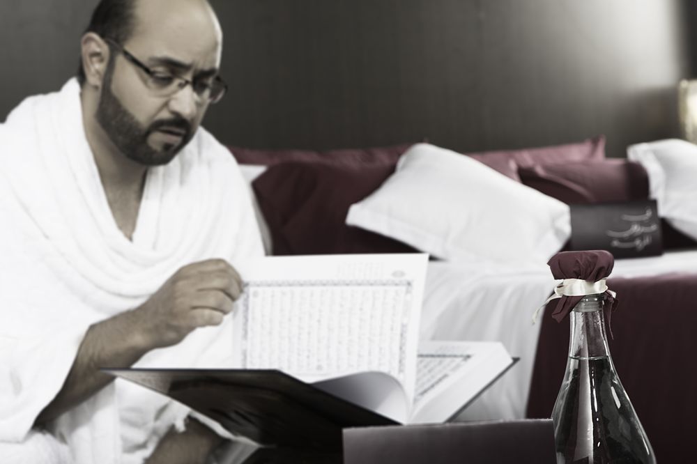 Makarem Ajyad Makkah Hotel Мека Екстериор снимка The photo shows a man engaged in reading a book or document, seated in a room with a relaxed atmosphere. He is wearing traditional white attire, often associated with specific cultural or religious practices. In the foreground, there is a bottle, pos